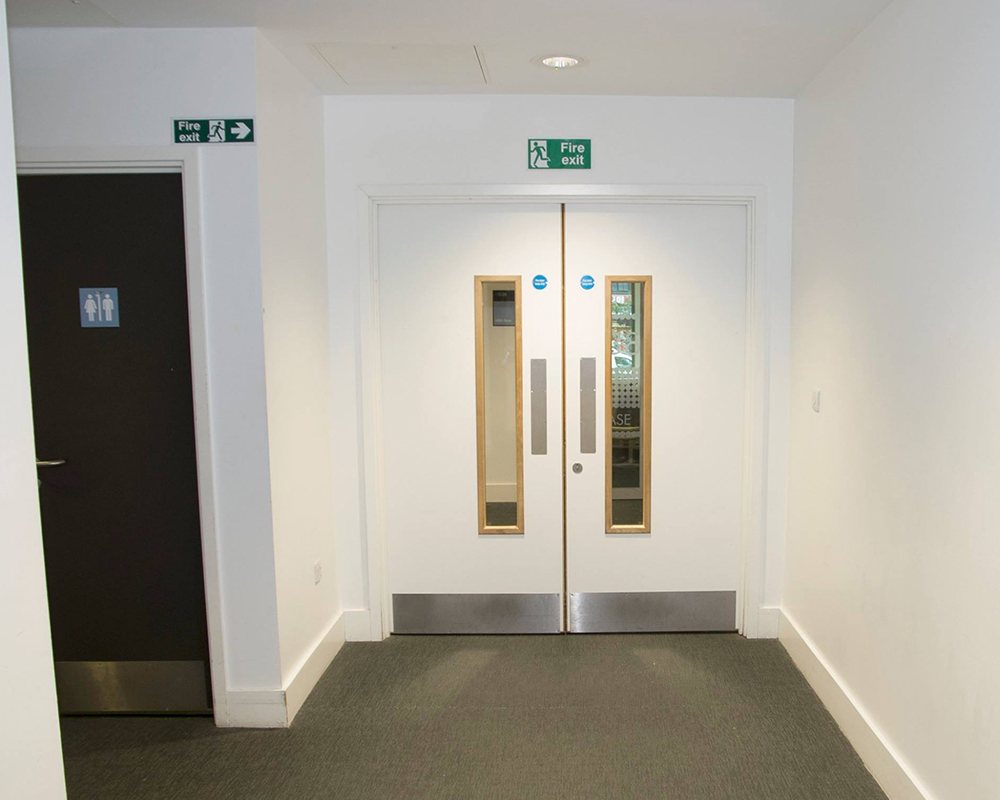 Installed white double doors with glazed vision panels and metal kick plates in a commercial corridor