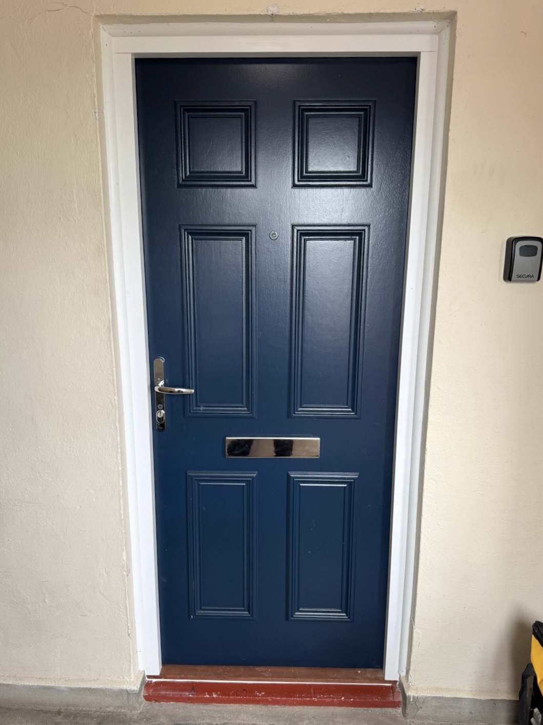 Installed blue six-panel residential entrance door with white frame, silver handle and letterplate